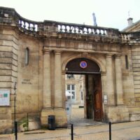 Grande porte cochère en bois sculpté dans une façade en pierre à Bordeaux.
