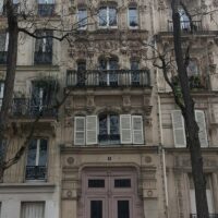 Façade en pierre d’un immeuble parisien avec fenêtres et balcons en ferronnerie.