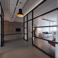 Couloir de bureaux bordé de cloisons vitrées à montants noirs, avec un espace salon sur la droite.