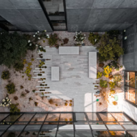 Vue plongeante d’une cour intérieure en béton avec cheminement, plantations et mobilier.