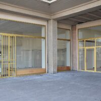 Vitrines aux encadrements jaunes d’un magasin vide sous une galerie en béton au Havre.
