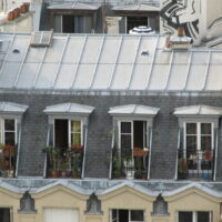 Quatre lucarnes sous un toit mansardé en zinc et ardoise à Paris.