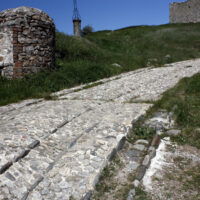 Chemin pavé bordé d’herbe et d’un ancien puits en pierre au château de Portes.