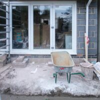 Chantier de travaux privatifs devant une façade vitrée, avec échafaudage et brouette.