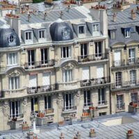 Façades parisiennes en pierre avec plusieurs étages de fenêtres, des balcons et des toitures à lucarnes.