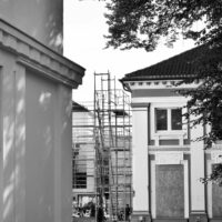 Échafaudage entre des façades anciennes, photographié en noir et blanc.